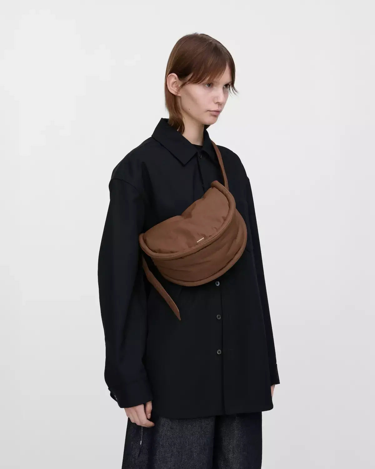 Model showcasing Curve Crossbody Round S Dark Taupe Shoulder Bag, stylish and lightweight with padded strap.