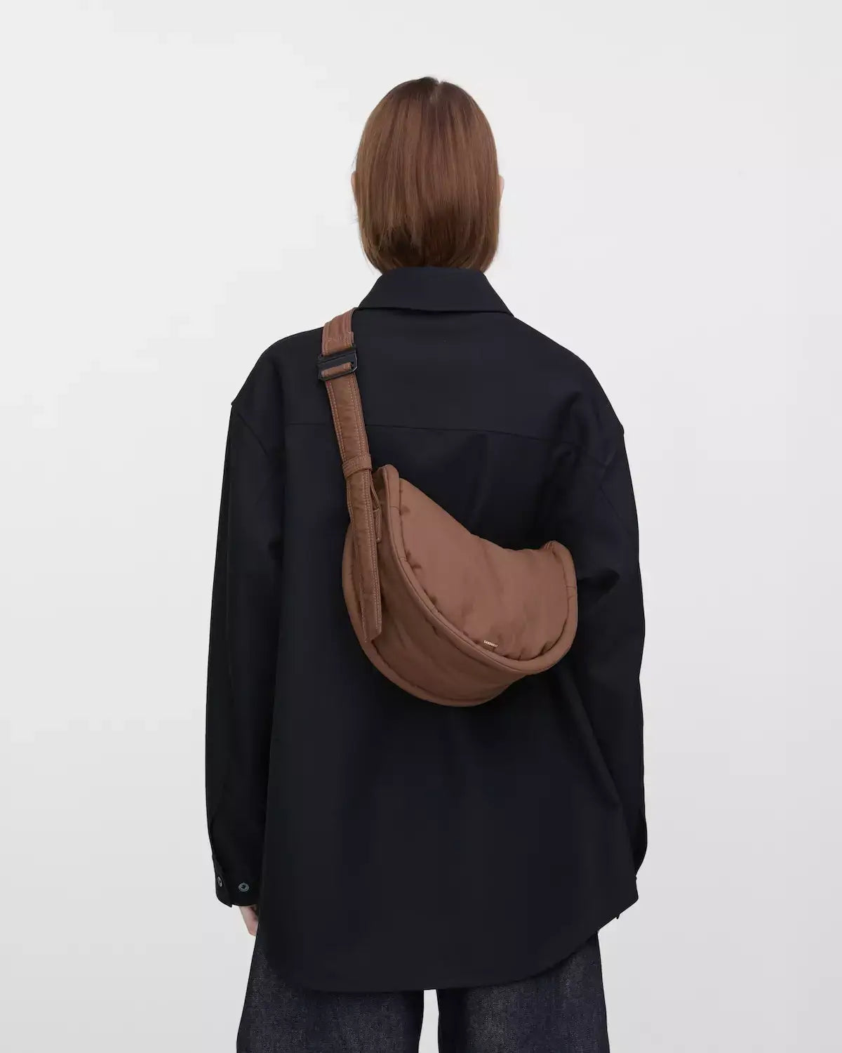 Curve Crossbody Round S Dark Taupe Shoulder Bag worn cross-body against a black shirt.
