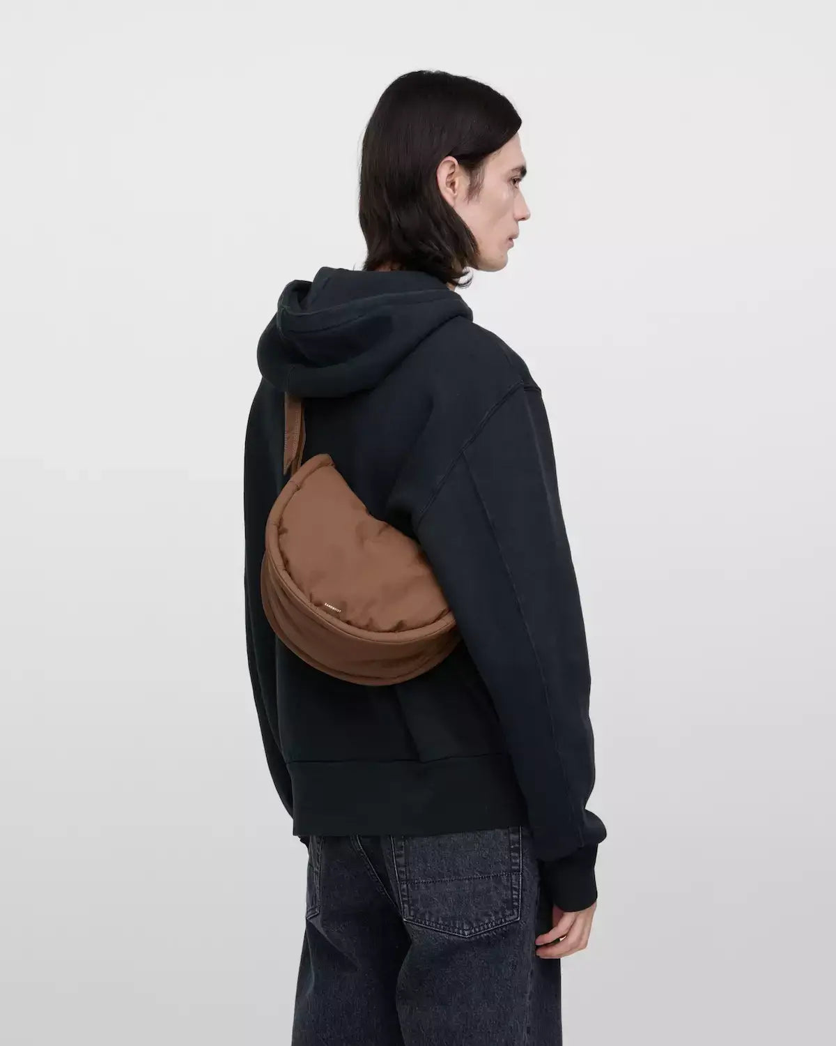 Model wearing Curve Crossbody Round S Dark Taupe Shoulder Bag casually over a hoodie.