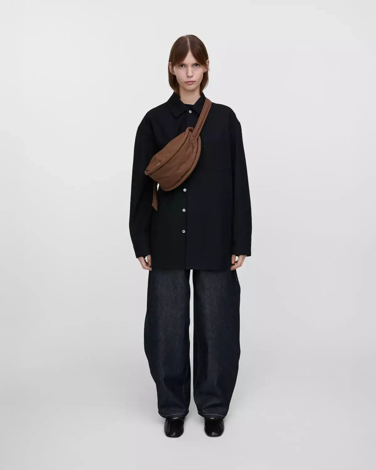 Model wearing Curve Crossbody Round S Dark Taupe Shoulder Bag with oversized shirt and wide-leg jeans.