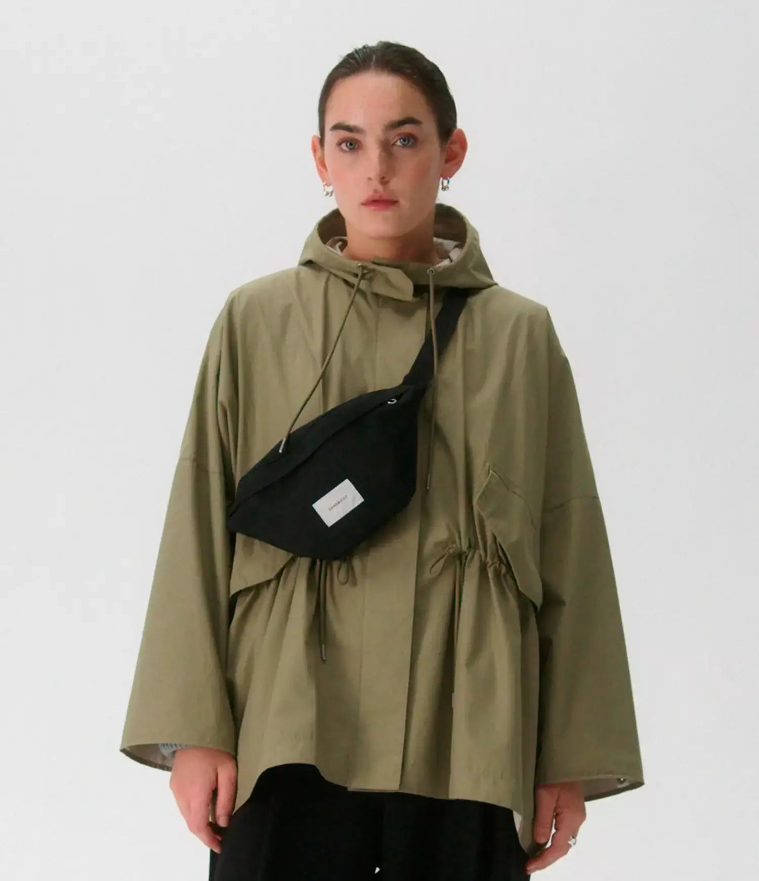 Model wearing Ground Crossbody Bag Black Bum Bag with stylish jacket in a minimalistic setting.