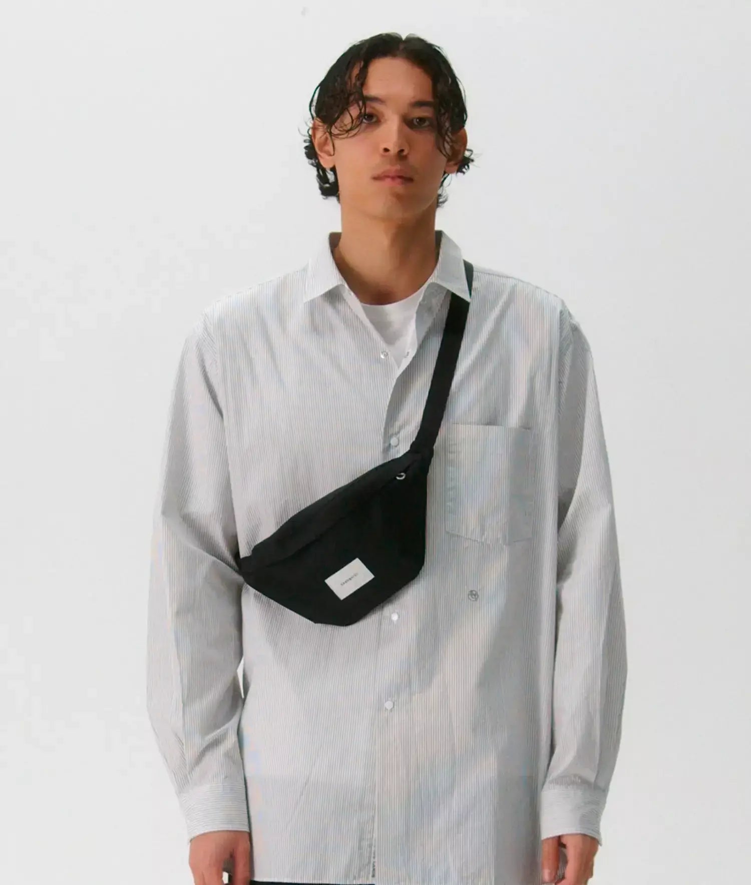 Model wearing Ground Crossbody Bag Black Bum Bag with adjustable strap over a white shirt.