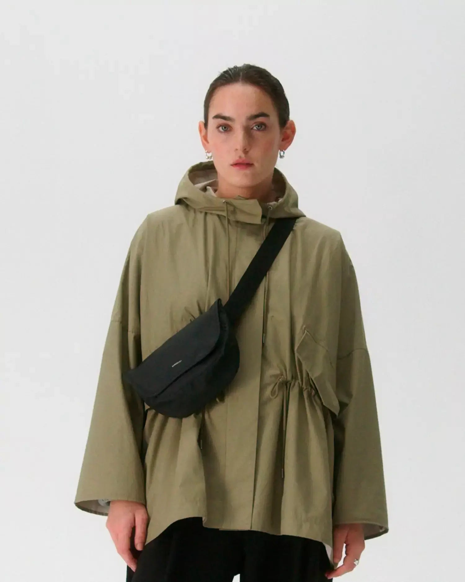 Woman wearing an olive green jacket with Stream Messenger Mini Black Shoulder Bag across her body.