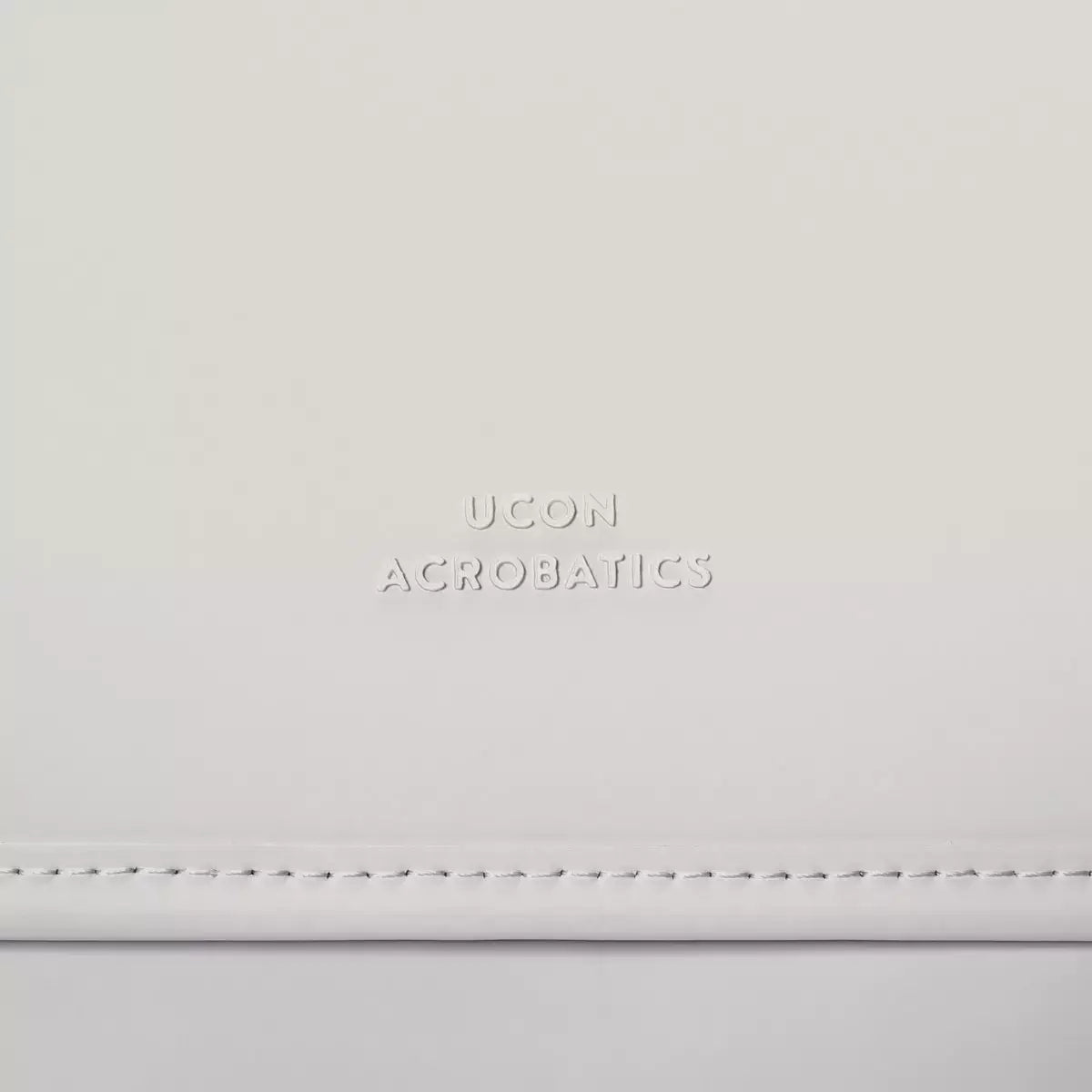 Close-up of UCON Acrobatics logo embossed on white material, showcasing minimalist design.