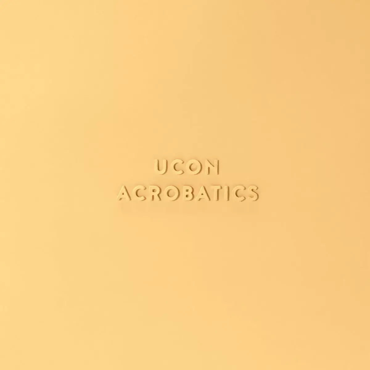 Close-up of UCON Acrobatics logo in a subtle embossed design on a yellow background.