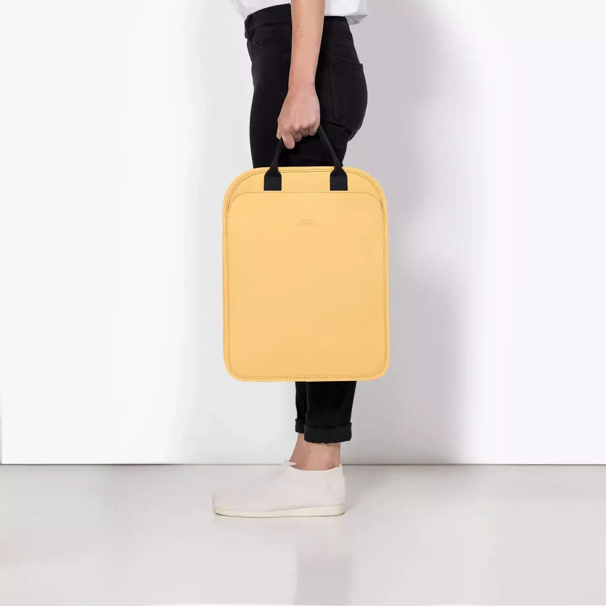 Alison Lotus Infinity Lemon Backpack being held, showcasing its stylish design and portable size.