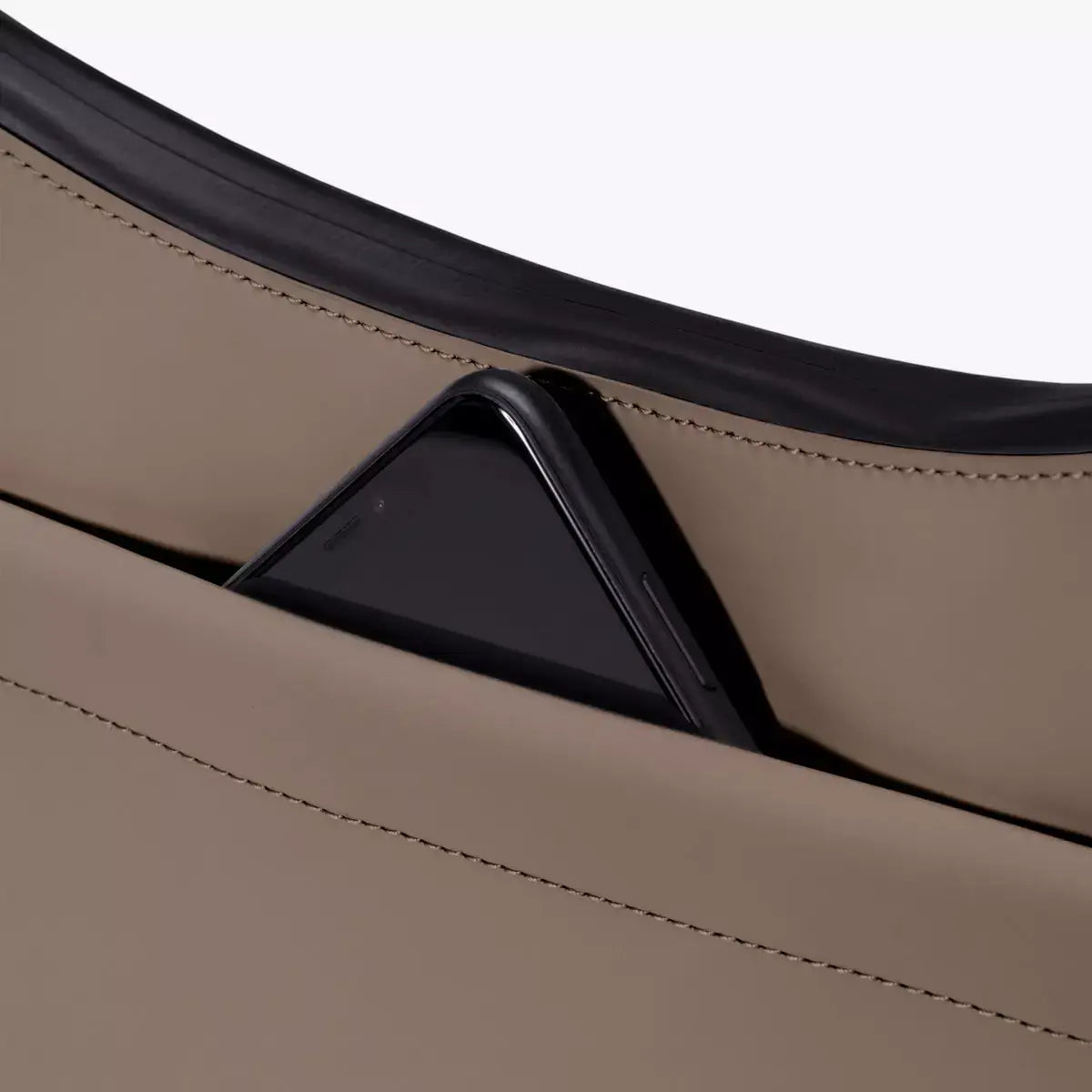 Close-up view of Alva Medium Lotus Infinity Dark Sand Shoulder Bag with a smartphone in the front pocket.