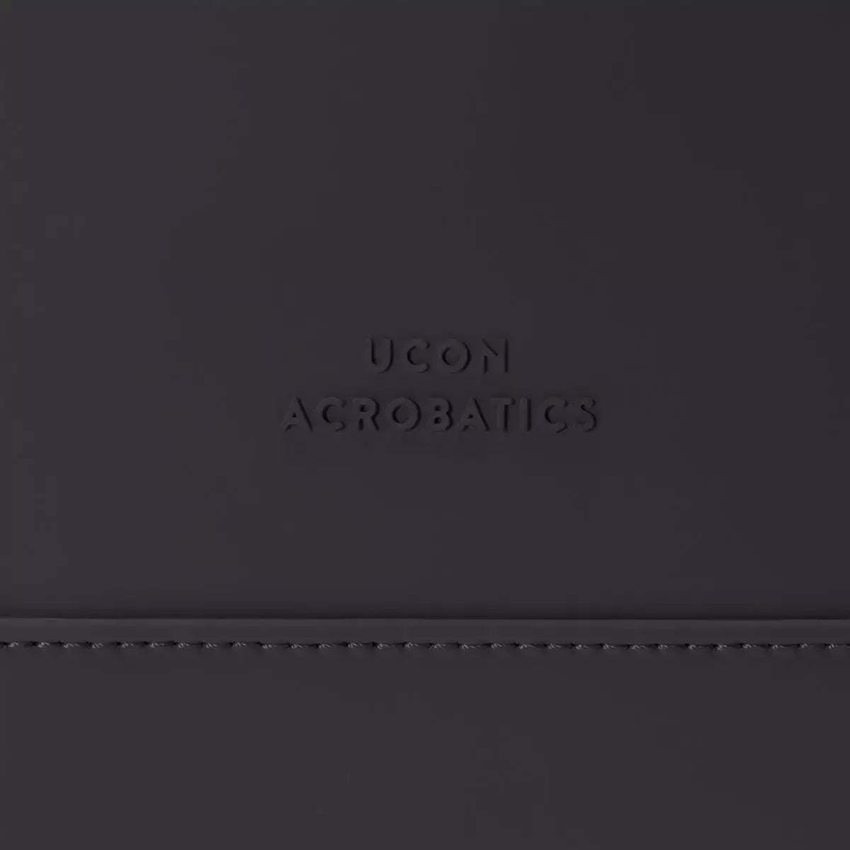 Close-up of UCON Acrobatics logo on a sleek, black material showcasing modern design and branding.