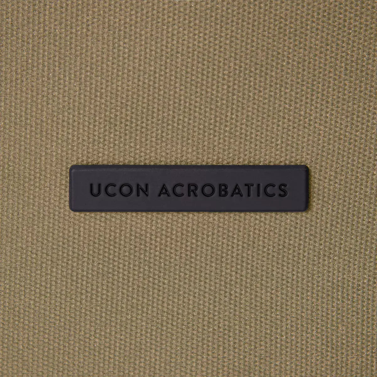UCON ACROBATICS logo on a khaki fabric background, showcasing a stylish backpack design.