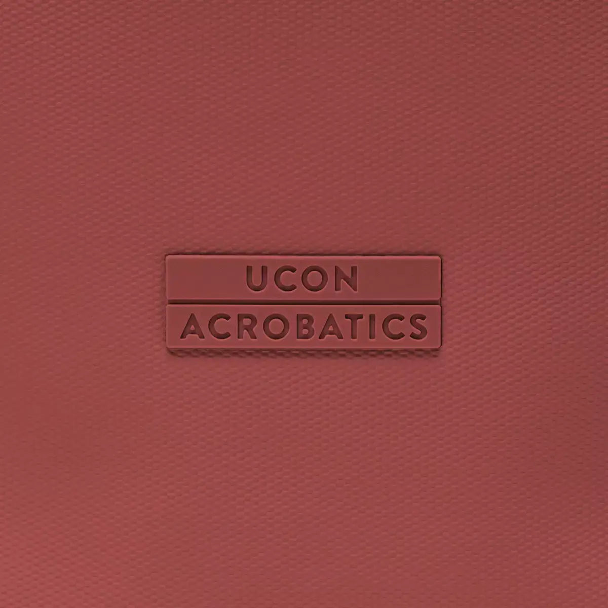 UCON ACROBATICS logo embossed on a textured red surface, showcasing brand identity and design.