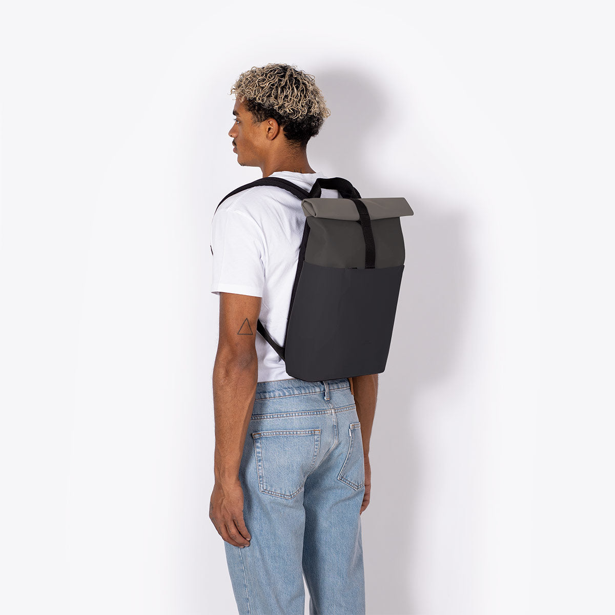 Hajo Mini Lotus Asphalt Black Backpack worn by a person with curly hair, showcasing its stylish roll-top design.