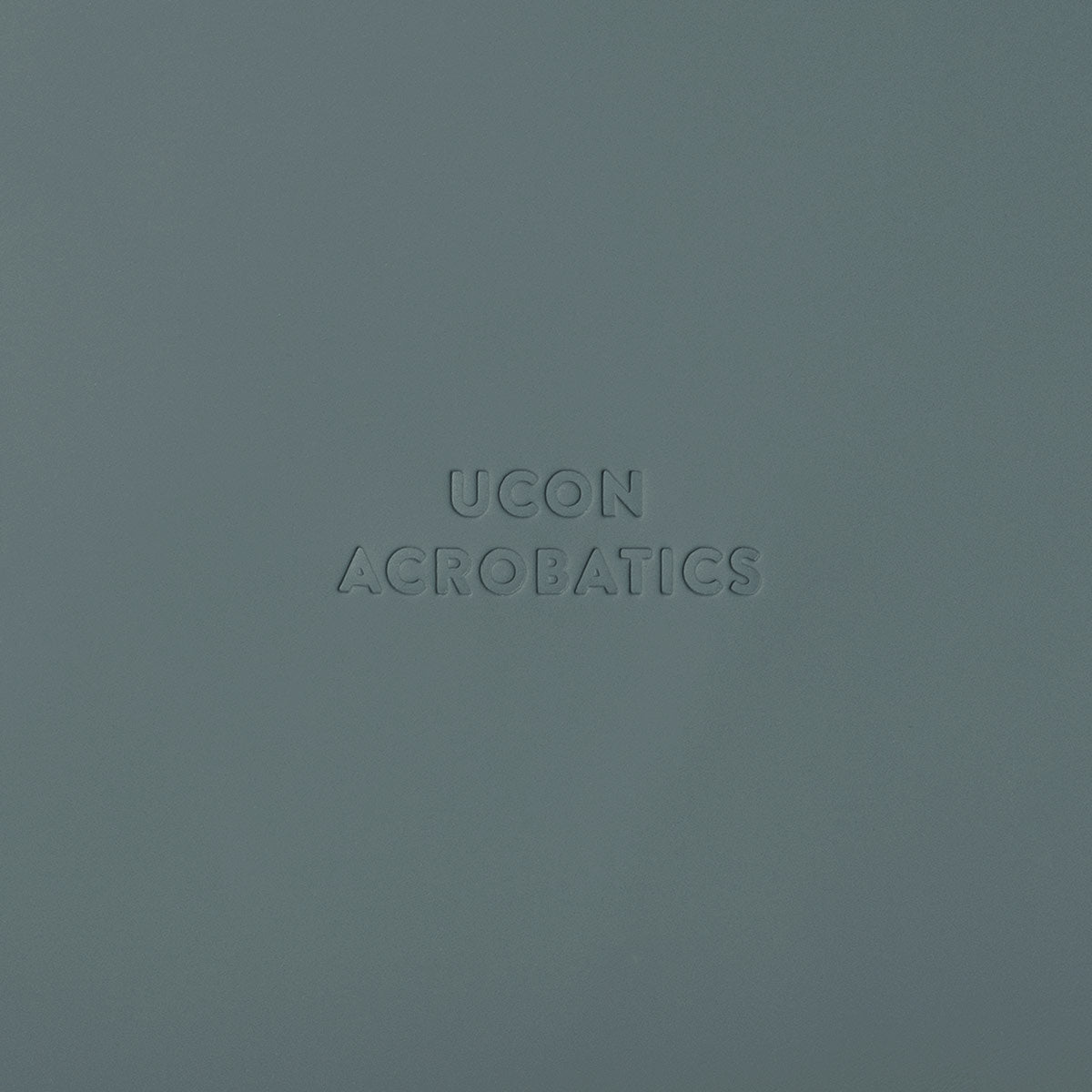 UCON Acrobatics logo embossed on a textured green background, showcasing brand identity and design aesthetic.