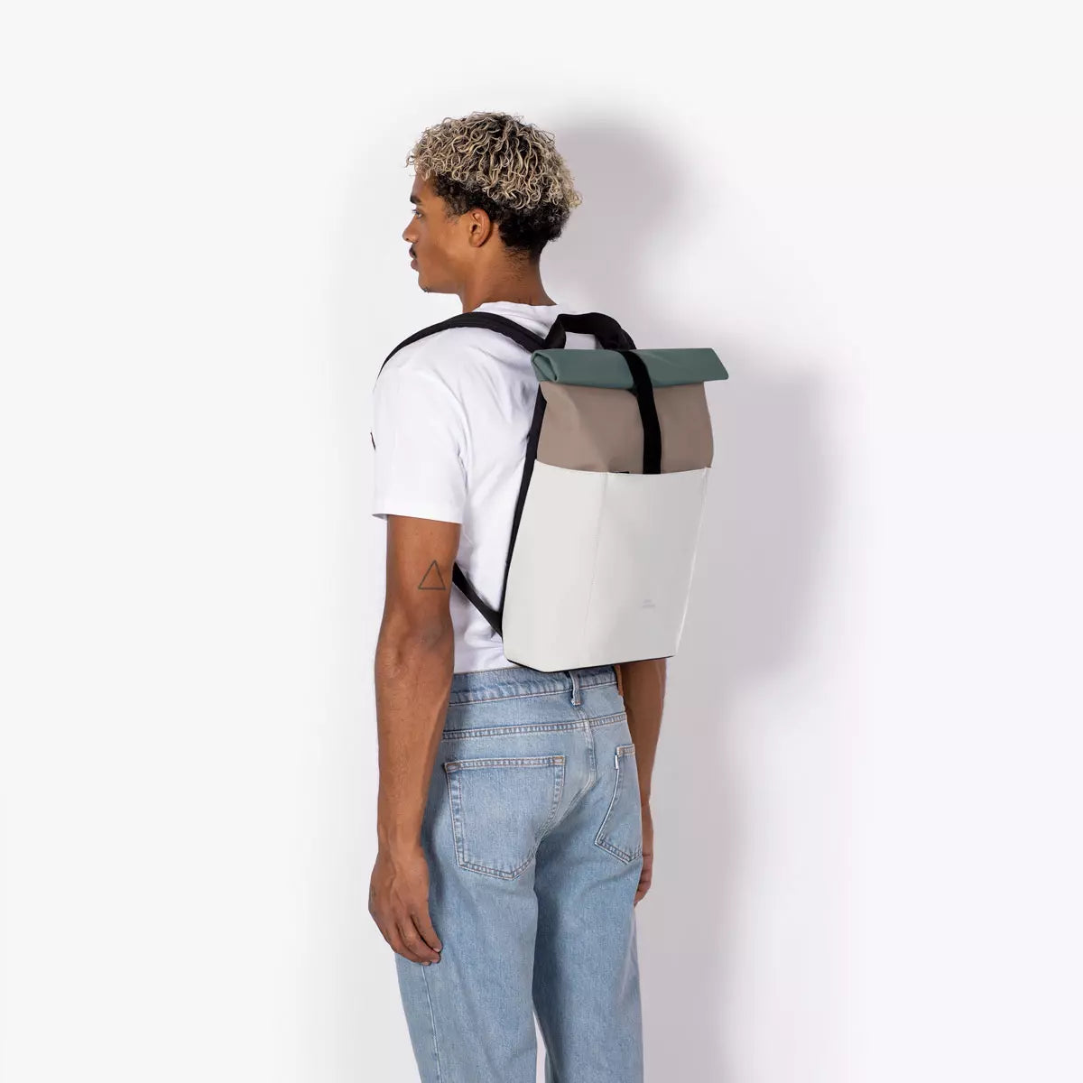Hajo Mini Lotus Infinity Dark Sand Glacier Grey Backpack worn by a man with curly hair.