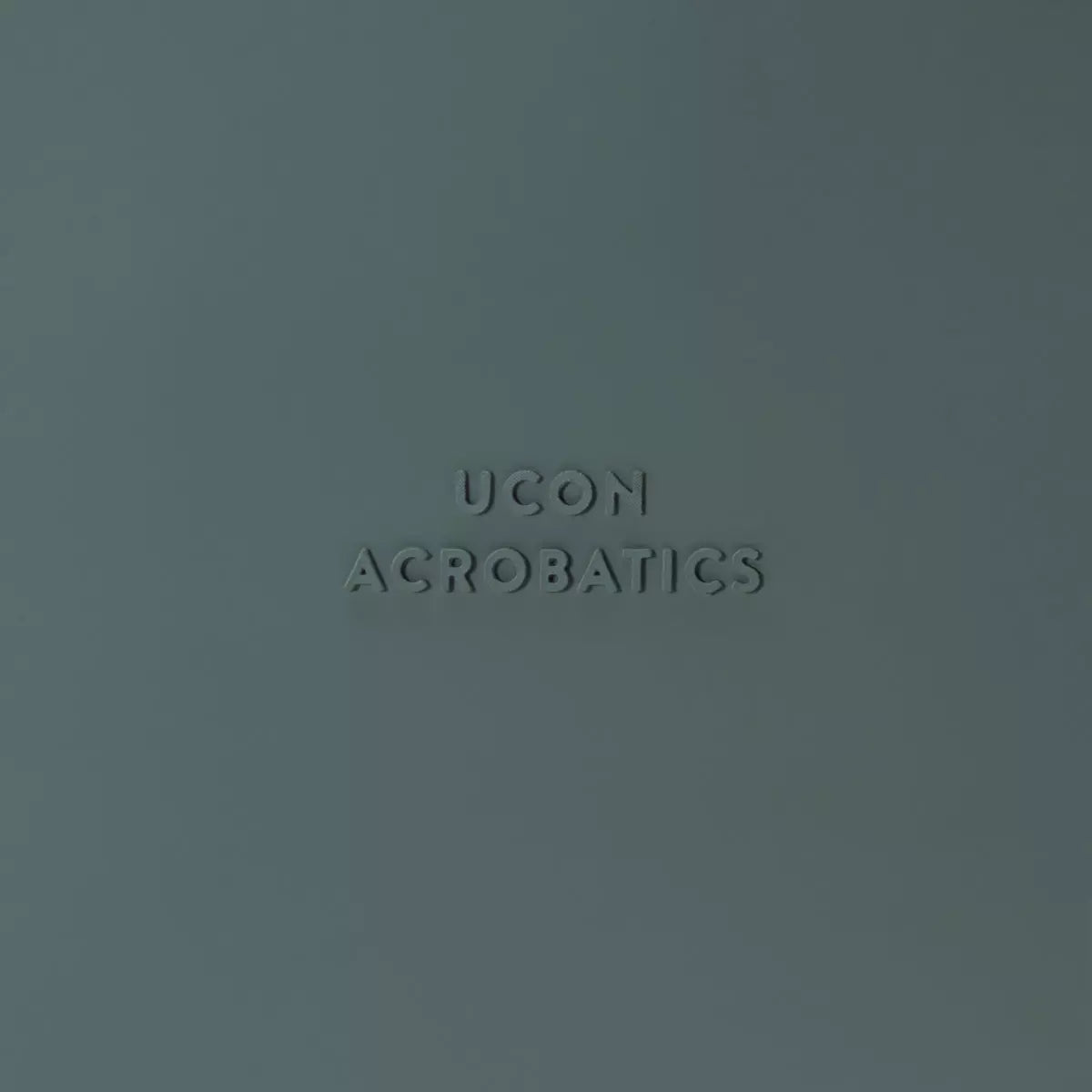 Close-up of UCON Acrobatics logo embossed on a textured dark green background.
