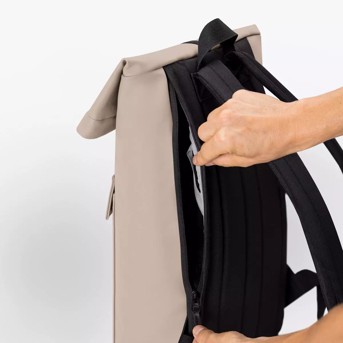 Jannik Mini Lotus Infinity Sand Backpack with a side zipper and roll-top closure being opened by a hand.