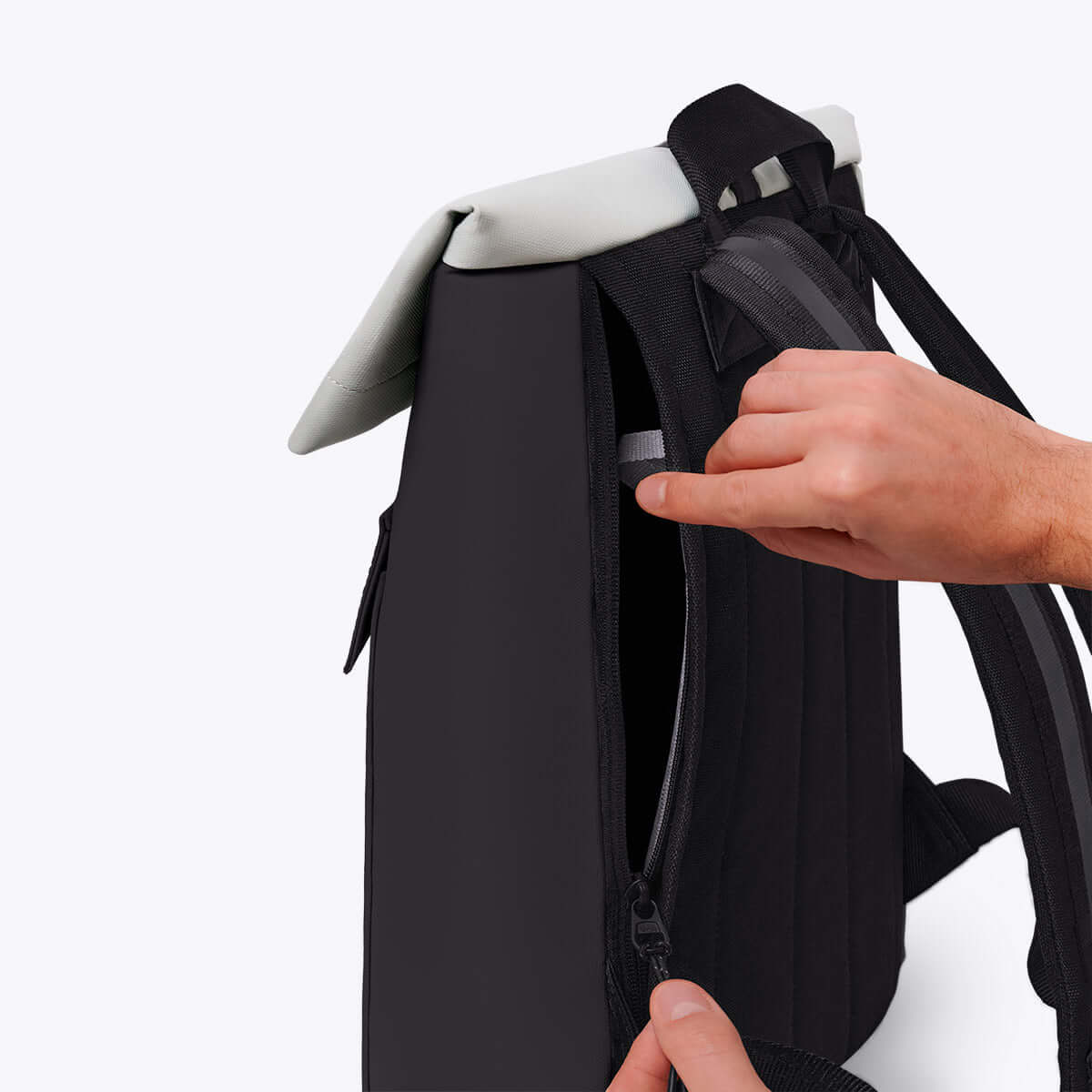 Jasper Aloe Black Backpack showcasing side zipper and roll-top design with a person's hand adjusting it.