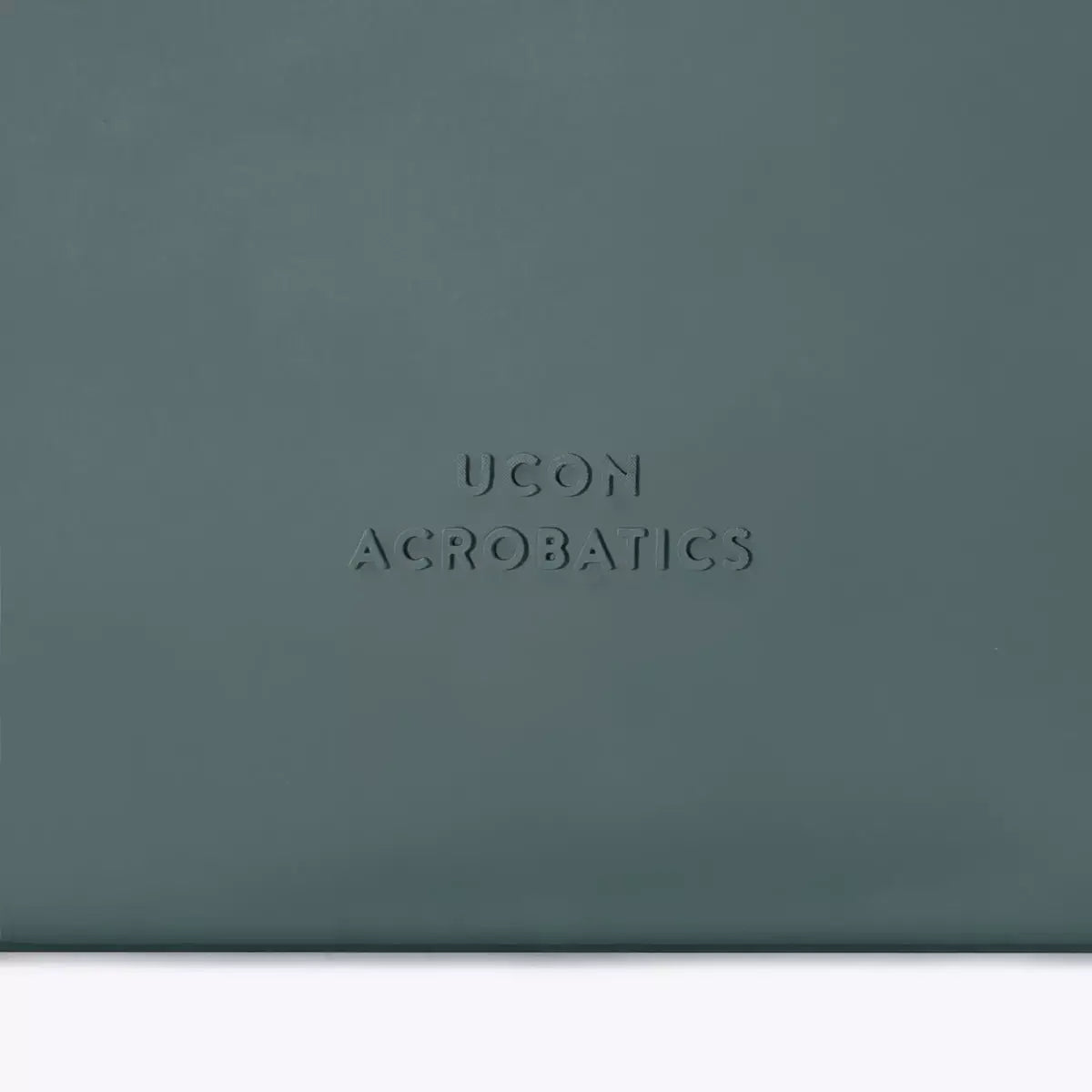 Ucon Acrobatics logo embossed on a dark green textured surface, showcasing brand style and quality.