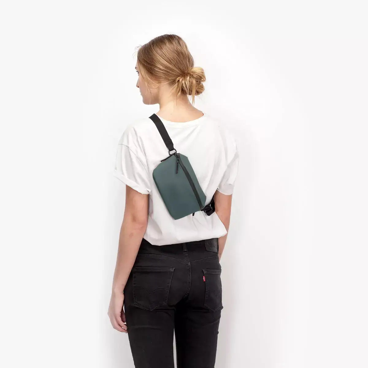 Woman wearing Jona Lotus Infinity Pine Green Bum Bag on her back, showcasing its sleek design and practicality.