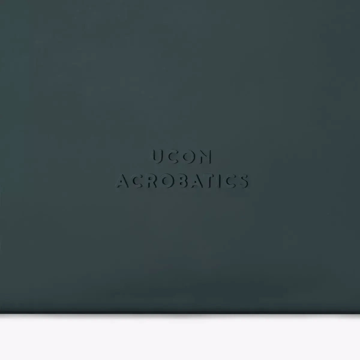 UCON AGROBATICS logo embossed on a dark green surface, showcasing brand identity and design.