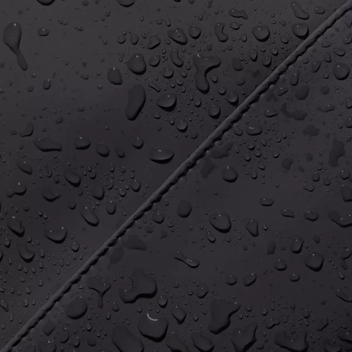 Close-up of waterproof surface on Yuto Medium Lotus Infinity Black Backpack with water droplets.