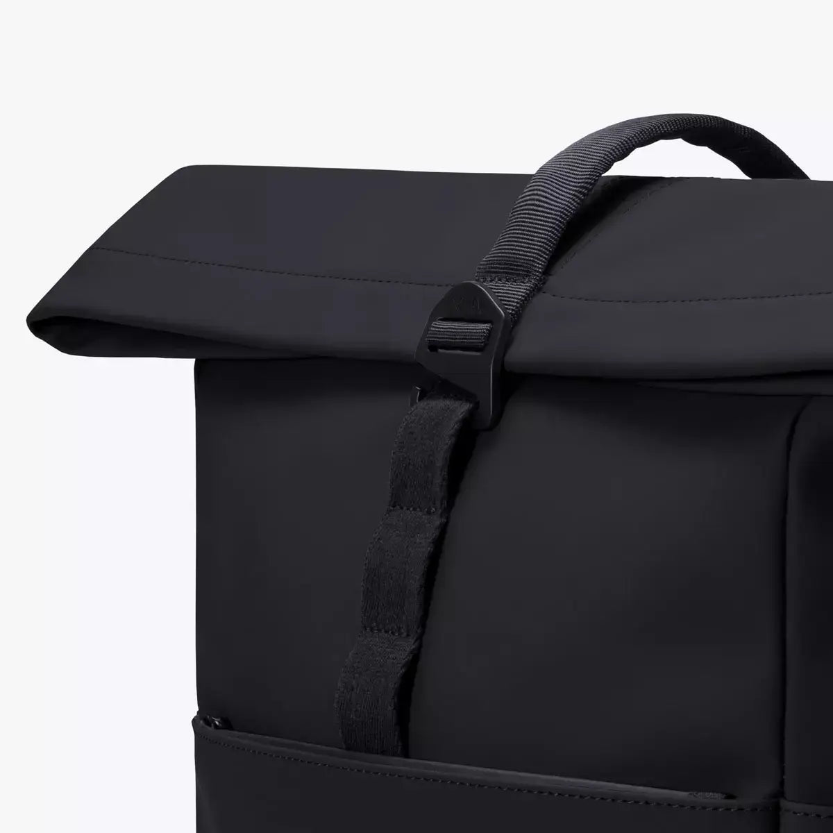 Yuto Medium Lotus Infinity Black Backpack close-up showing the top flap and strap detail.