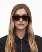Model wearing 05 Core Brown Sunglasses with a stylish black outfit, showcasing their durability and design.