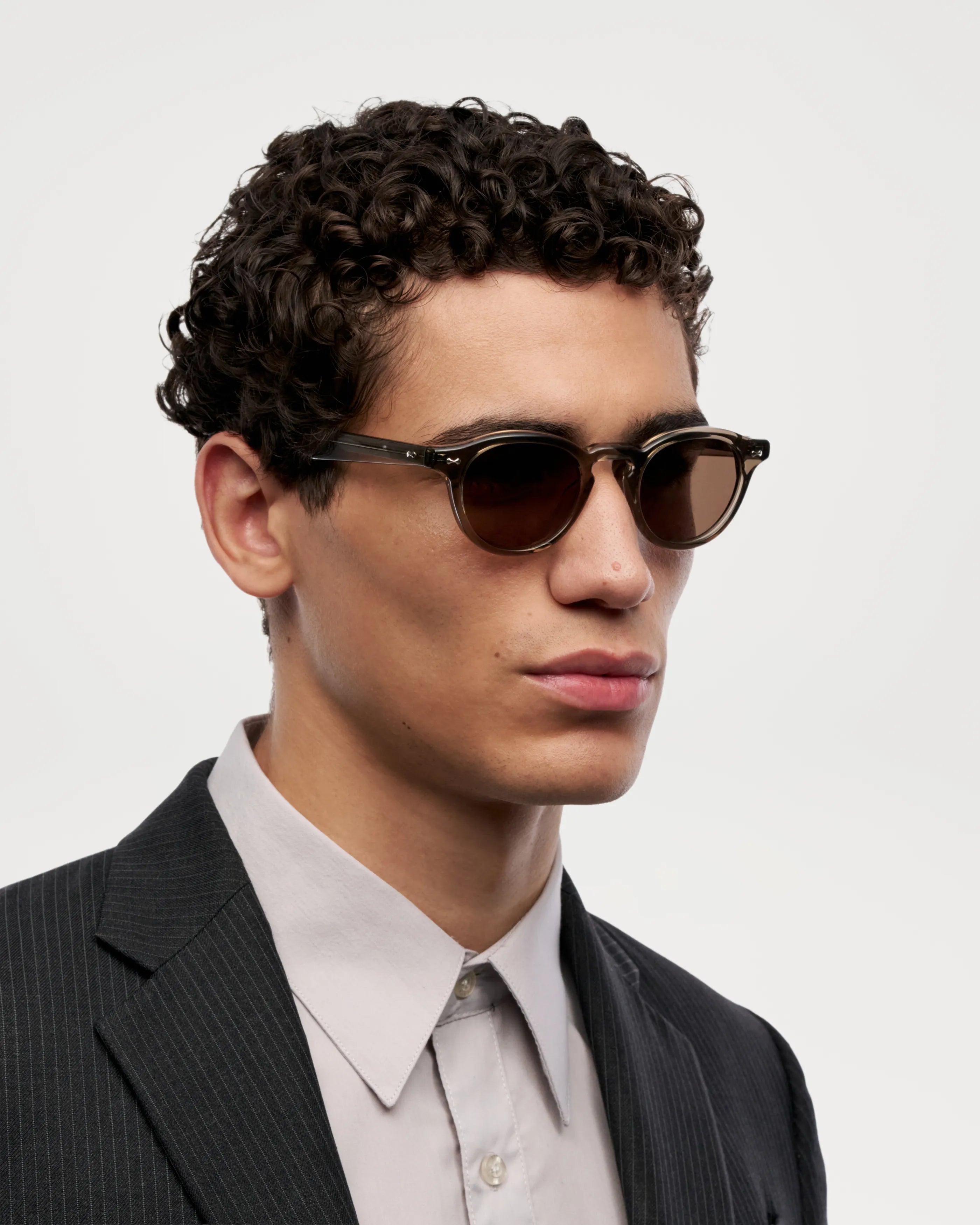 Model wearing Scope Light Taupe Sunglasses with a stylish suit, showcasing their modern design and high-quality build.