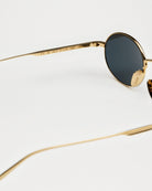 Close-up of Oval Gold Sunglasses featuring gold frame and dark lenses, emphasizing UV protection and eco-friendly materials.