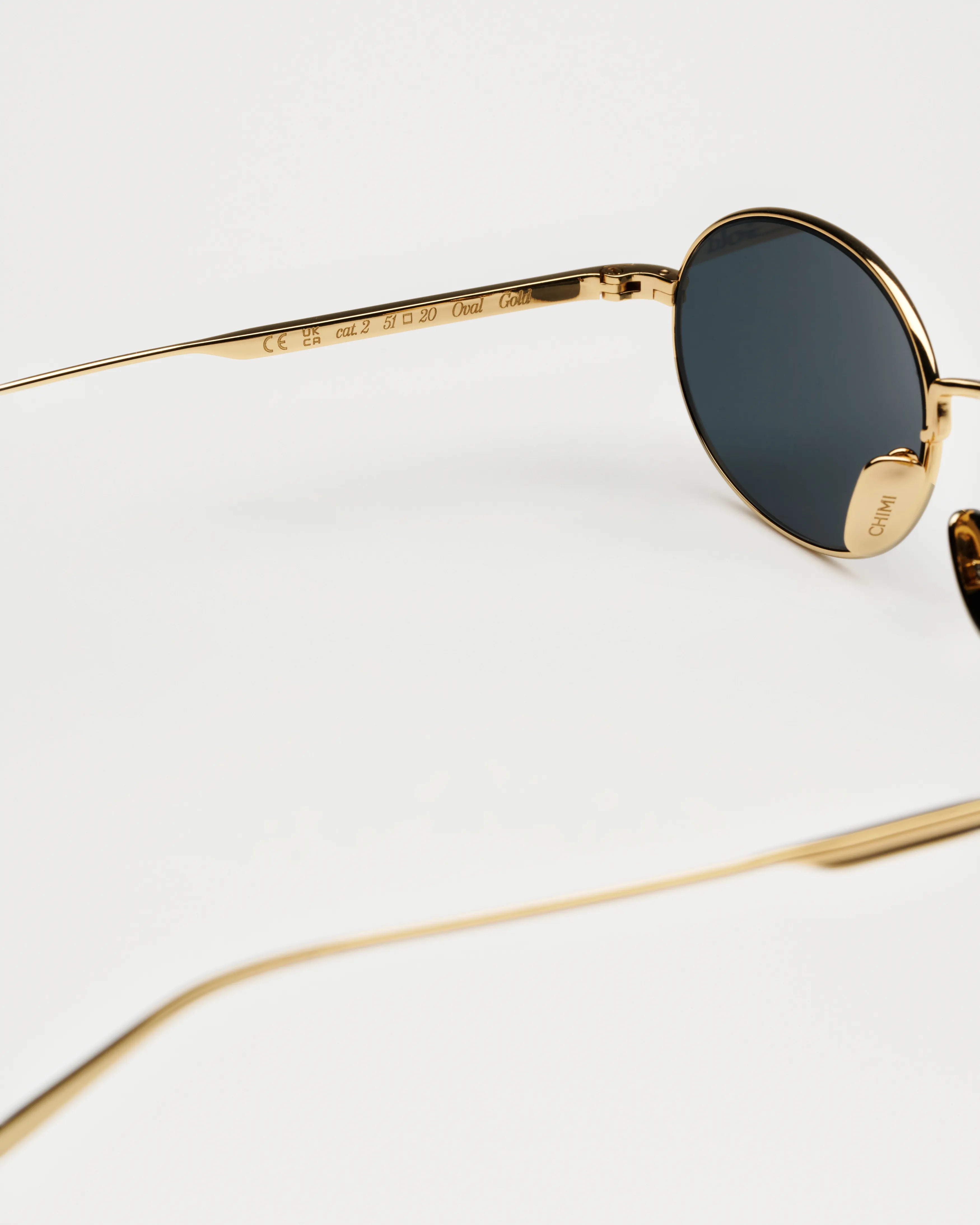 Close-up of Oval Gold Sunglasses featuring gold frame and dark lenses, emphasizing UV protection and eco-friendly materials.