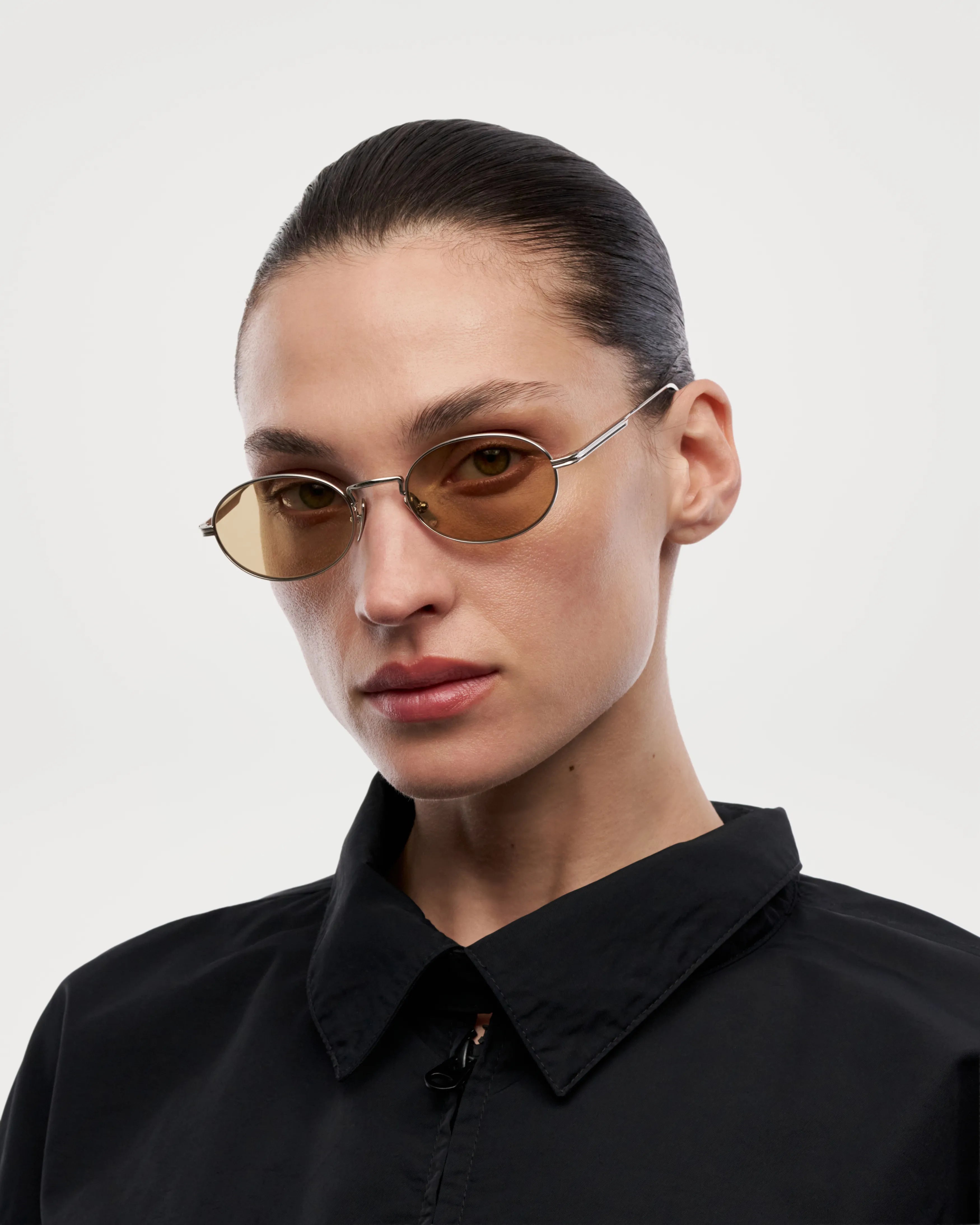 Model wearing Oval Silver Sunglasses with brown lenses, featuring a modern design in a monochrome outfit.
