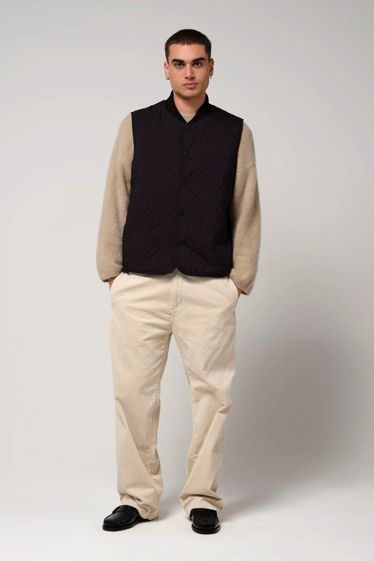 Model wearing a Claud Deep Black Coat with beige sleeves, paired with light-colored trousers and black shoes.
