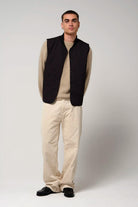 Model wearing a Claud Deep Black Coat vest, paired with a beige sweater and white pants, against a neutral background.