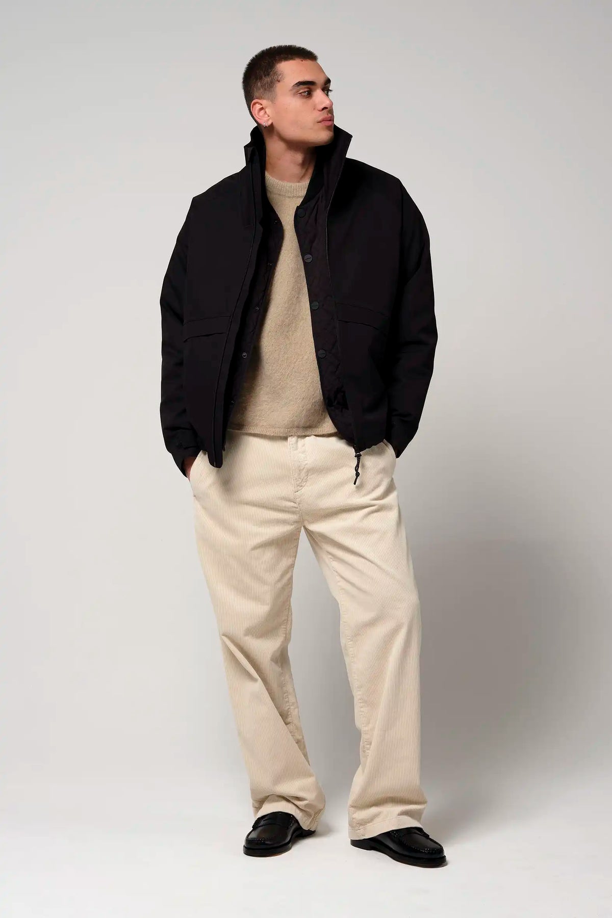 Man wearing the Claud Deep Black Coat styled with a beige sweater and light trousers, showcasing a fashionable outfit.