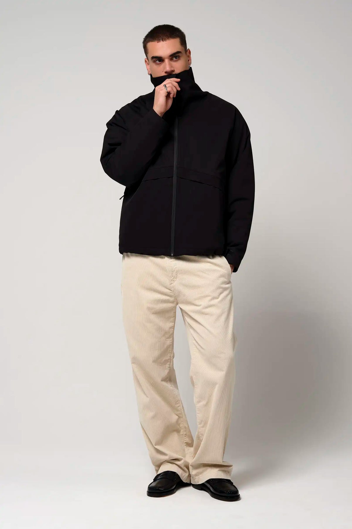 Man wearing Claud Deep Black Coat with a high collar, black jacket paired with light beige pants.