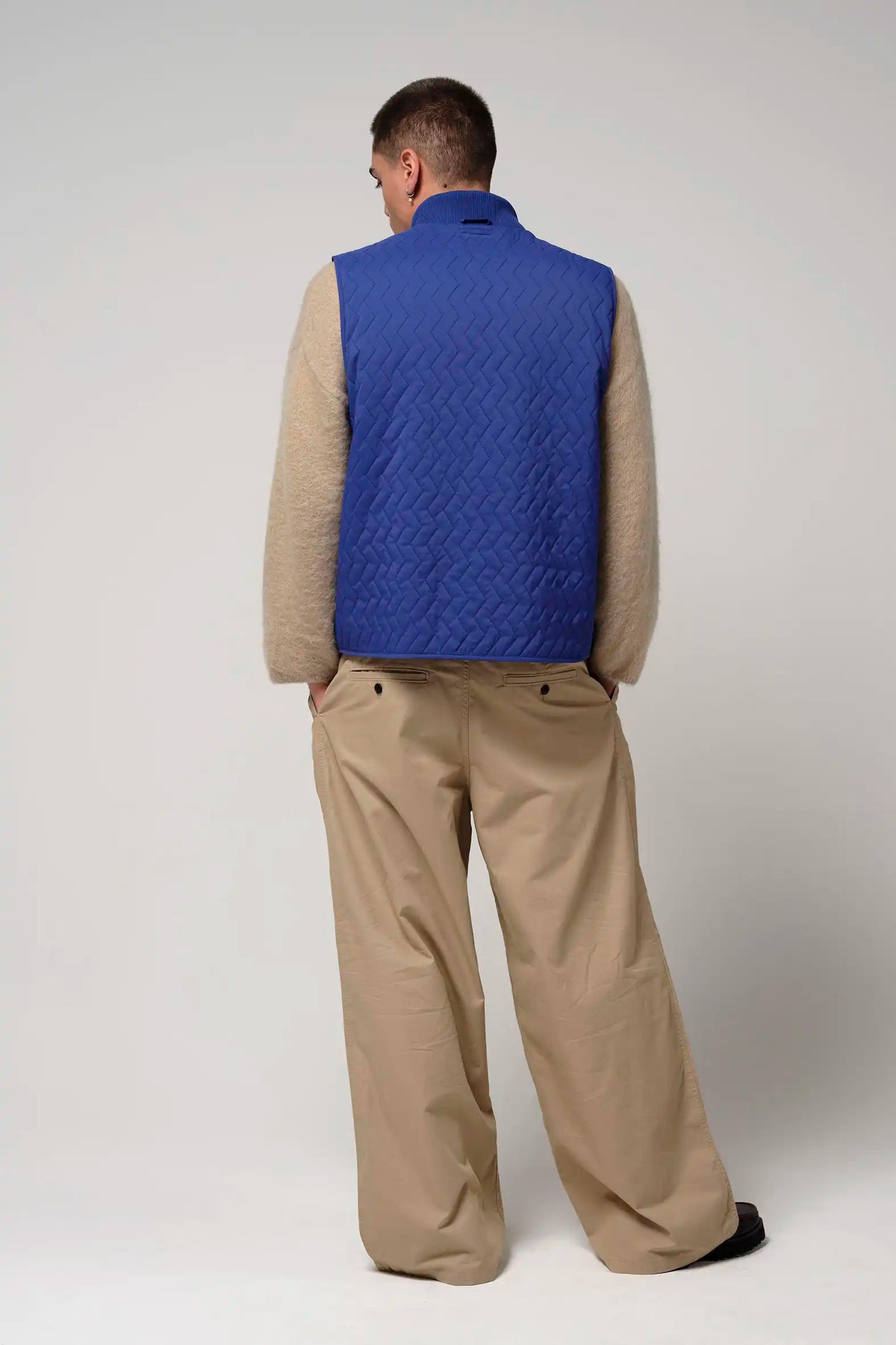 Model wearing Claud Sodalite Blue Coat from the back, featuring a quilted design and paired with beige pants.