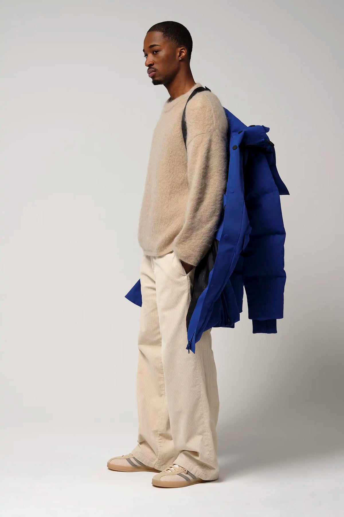 Model wearing a beige sweater and holding the Climate Sodalite Blue Coat, showcasing a modern, casual style.