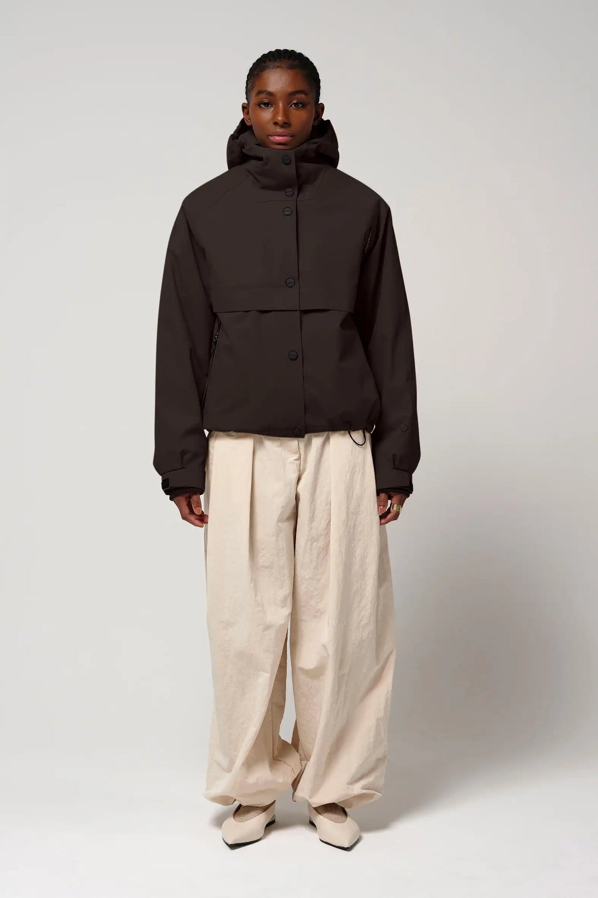 Model wearing Guthrie Black Coffee Coat, a waterproof and windproof jacket, styled with beige pants.