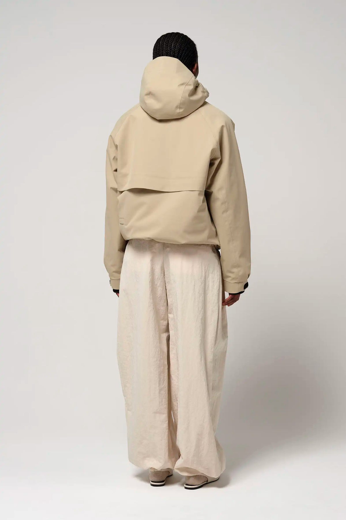 Back view of a person wearing the Guthrie Fields of Rye Beige Coat with adjustable hood and relaxed fit pants.