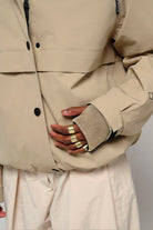 Guthrie Fields of Rye Beige Coat close-up showing adjustable cuff and hand with rings.