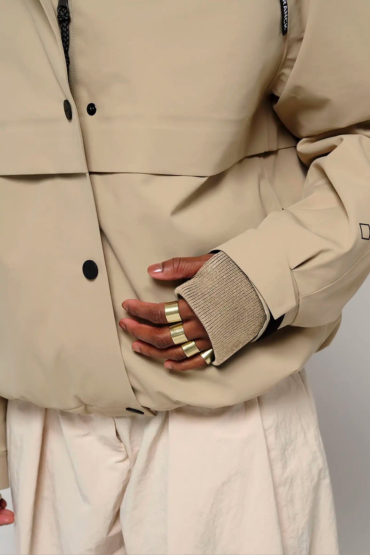 Guthrie Fields of Rye Beige Coat close-up showing adjustable cuff and hand with rings.