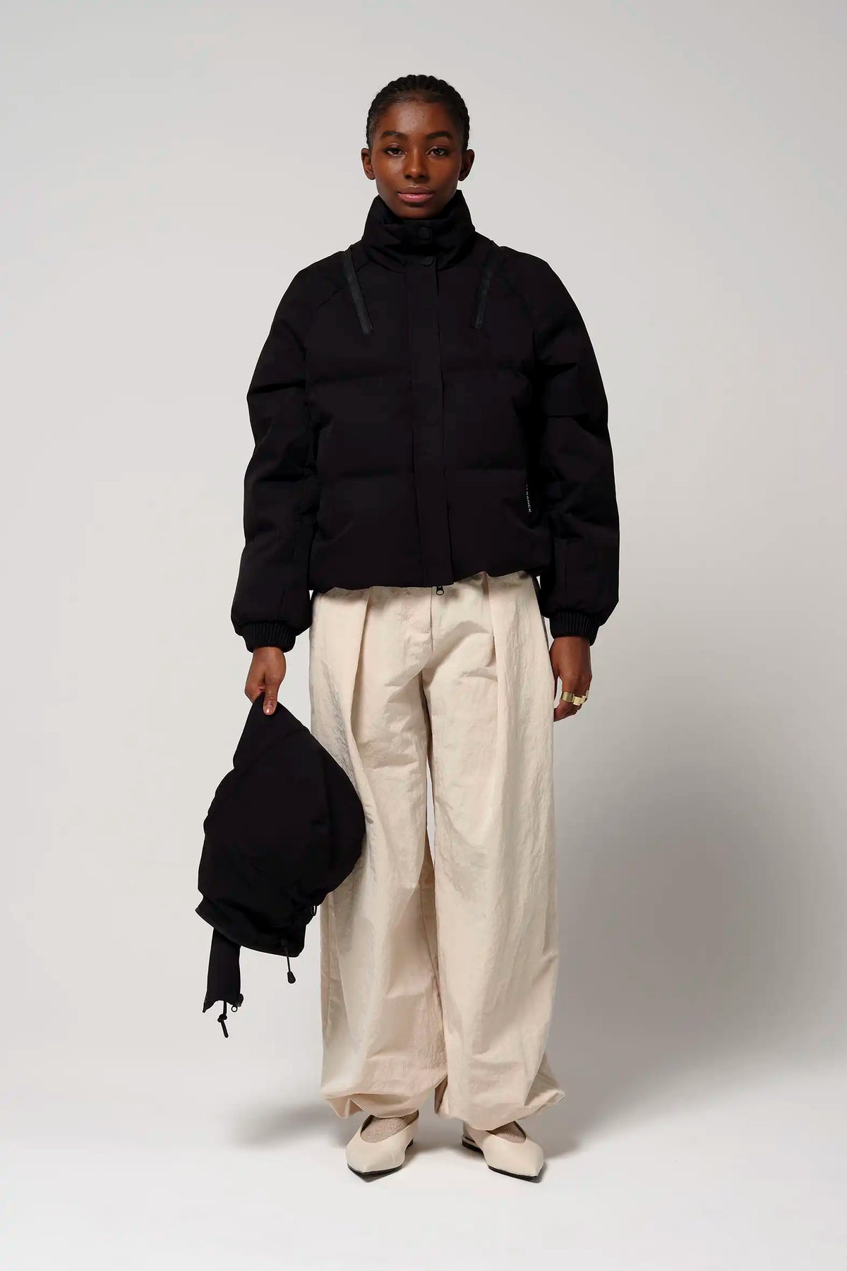 Model wearing the Talon Deep Black Coat with cream-colored wide pants and holding a black backpack.