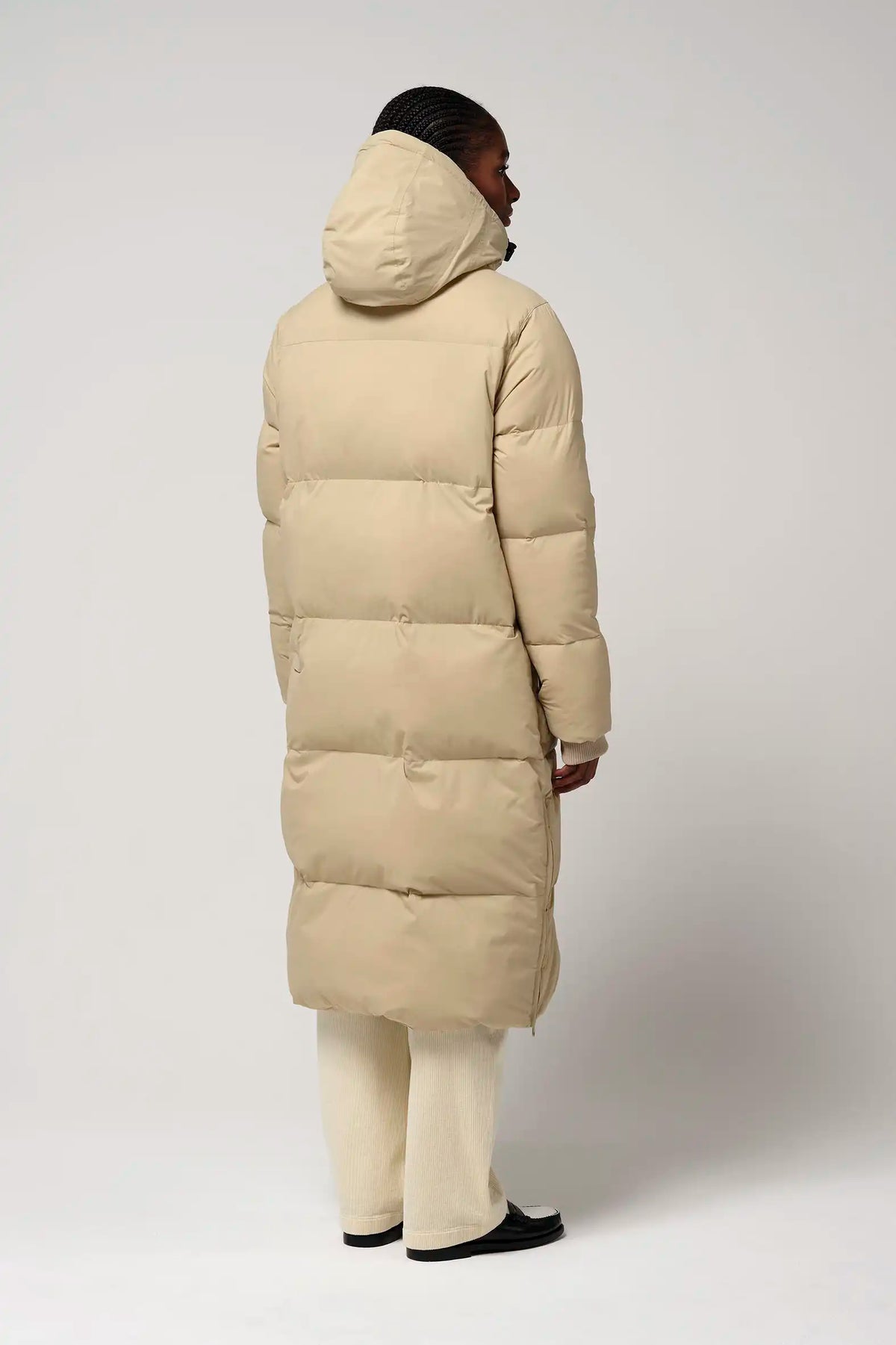 Model showing the back view of the Tsunami Fields of Rye Beige Coat, a lightweight waterproof puffer coat.