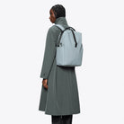 Clip Front Backpack Pool Backpack worn with a long coat, showcasing its stylish design and practical features.