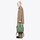 Clip Front Backpack Well Backpack in green, worn by a model in profile view, showcasing its modern design.