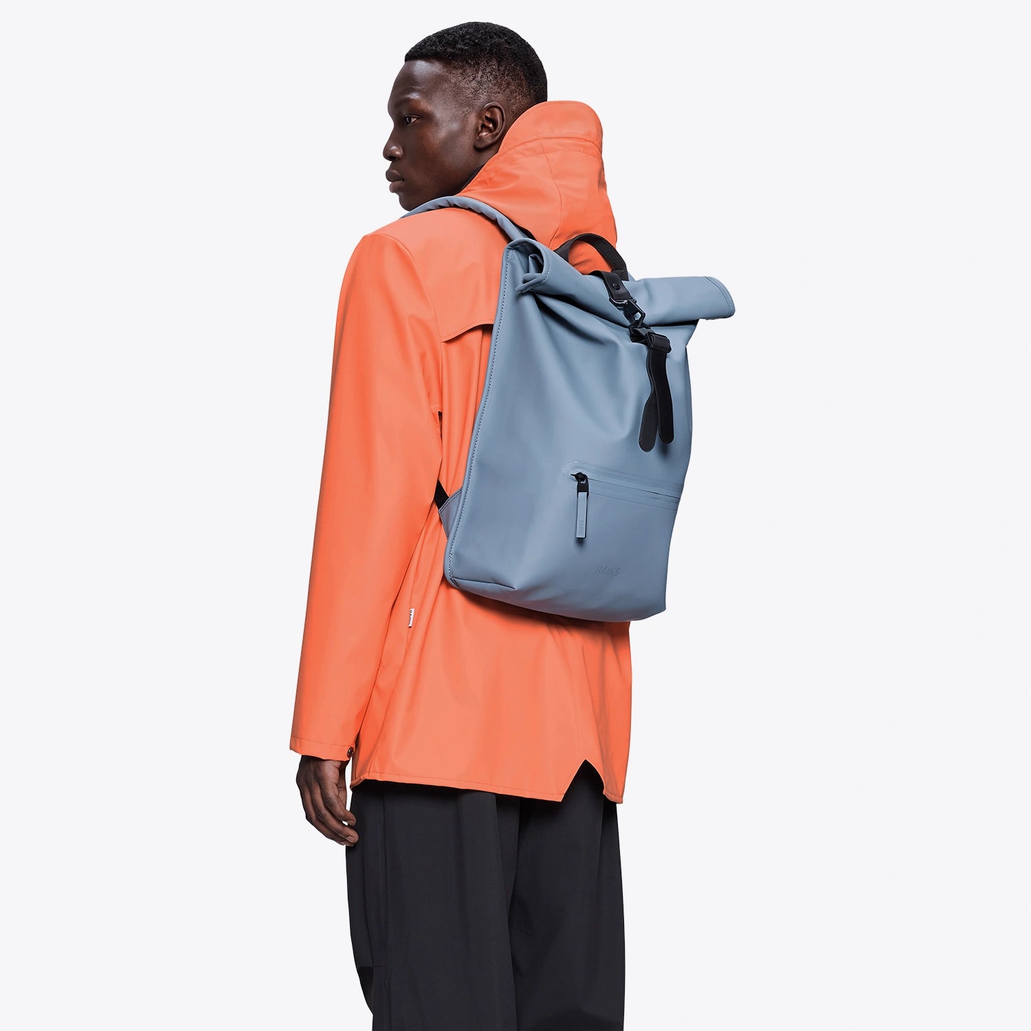 Person wearing an orange waterproof jacket with a Rolltop Rucksack Blue Dusk Backpack on their back.