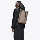 Man wearing a Rolltop Rucksack Cinder Backpack, showcasing its waterproof design and roll-top closure.