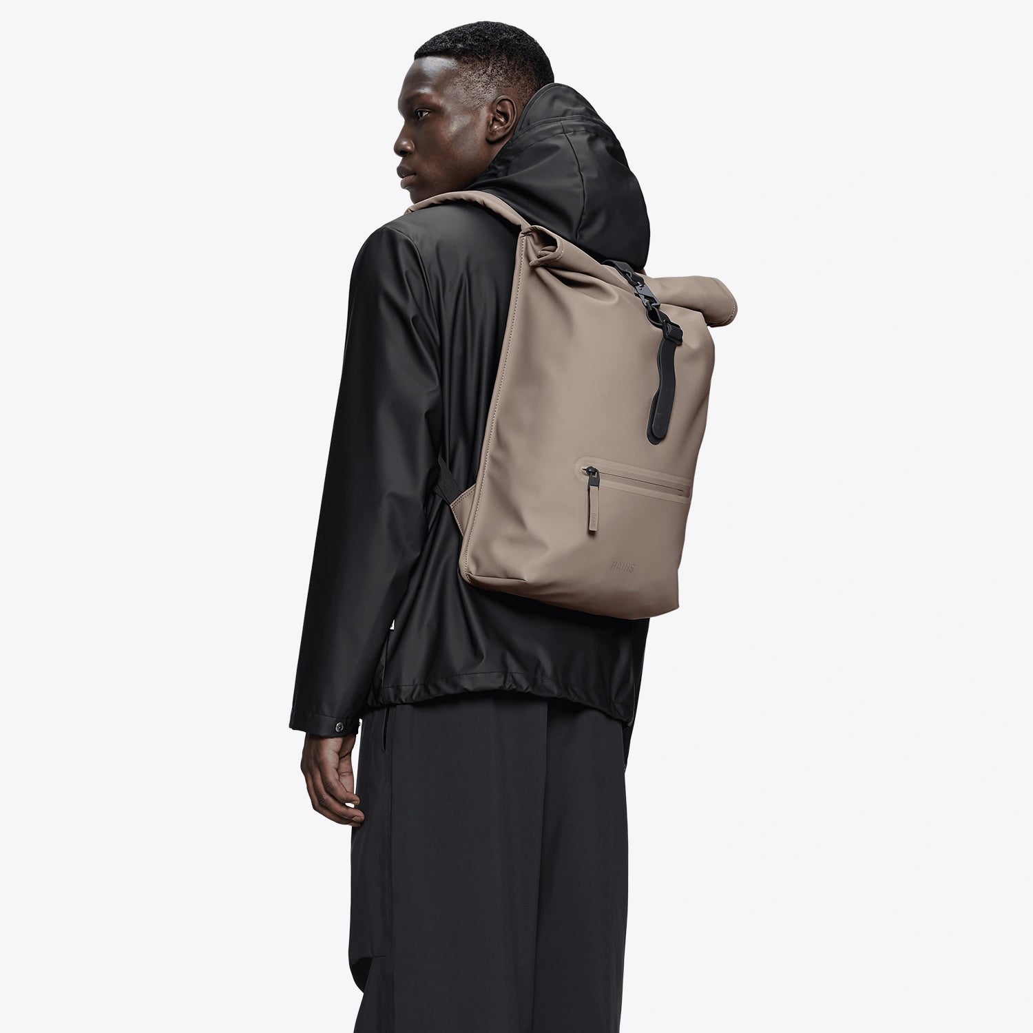Man wearing a Rolltop Rucksack Cinder Backpack, showcasing its waterproof design and roll-top closure.