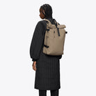 Woman wearing a Rolltop Rucksack Large Beige Backpack, showcasing its modern design and functionality.
