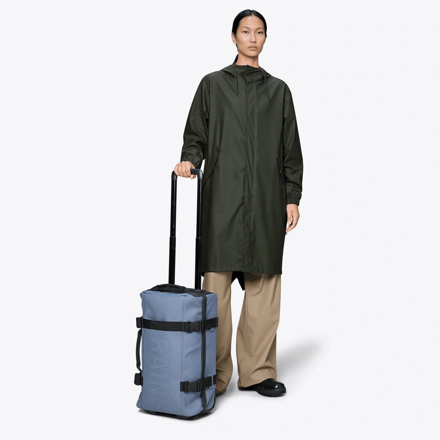 Texel Cabin Bag Small Blue Dusk Suitcase with a woman in a green raincoat holding it.