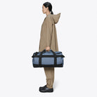Texel Duffel Bag Small Blue Dusk Duffel Backpack being held by a person in waterproof gear.